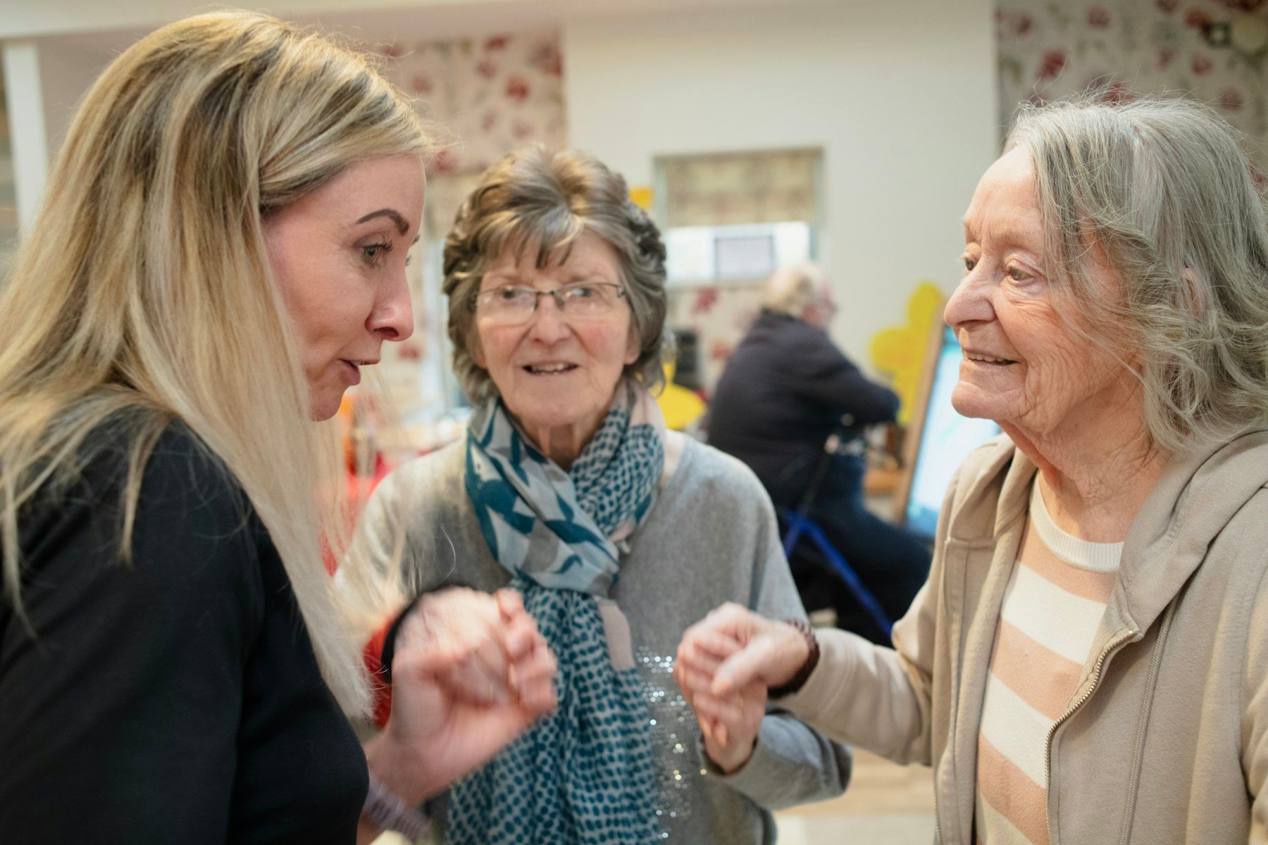 A caregiver chats with two older women in a lounge