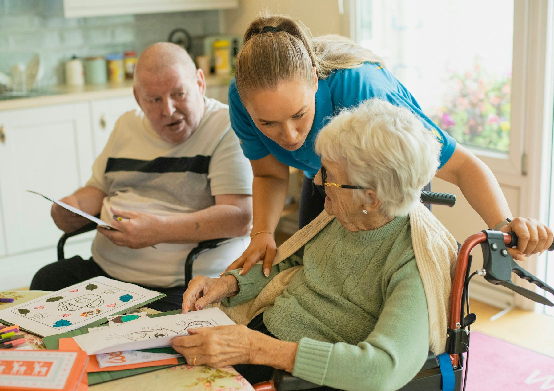 A caregiver leans in to help an older couple at a table