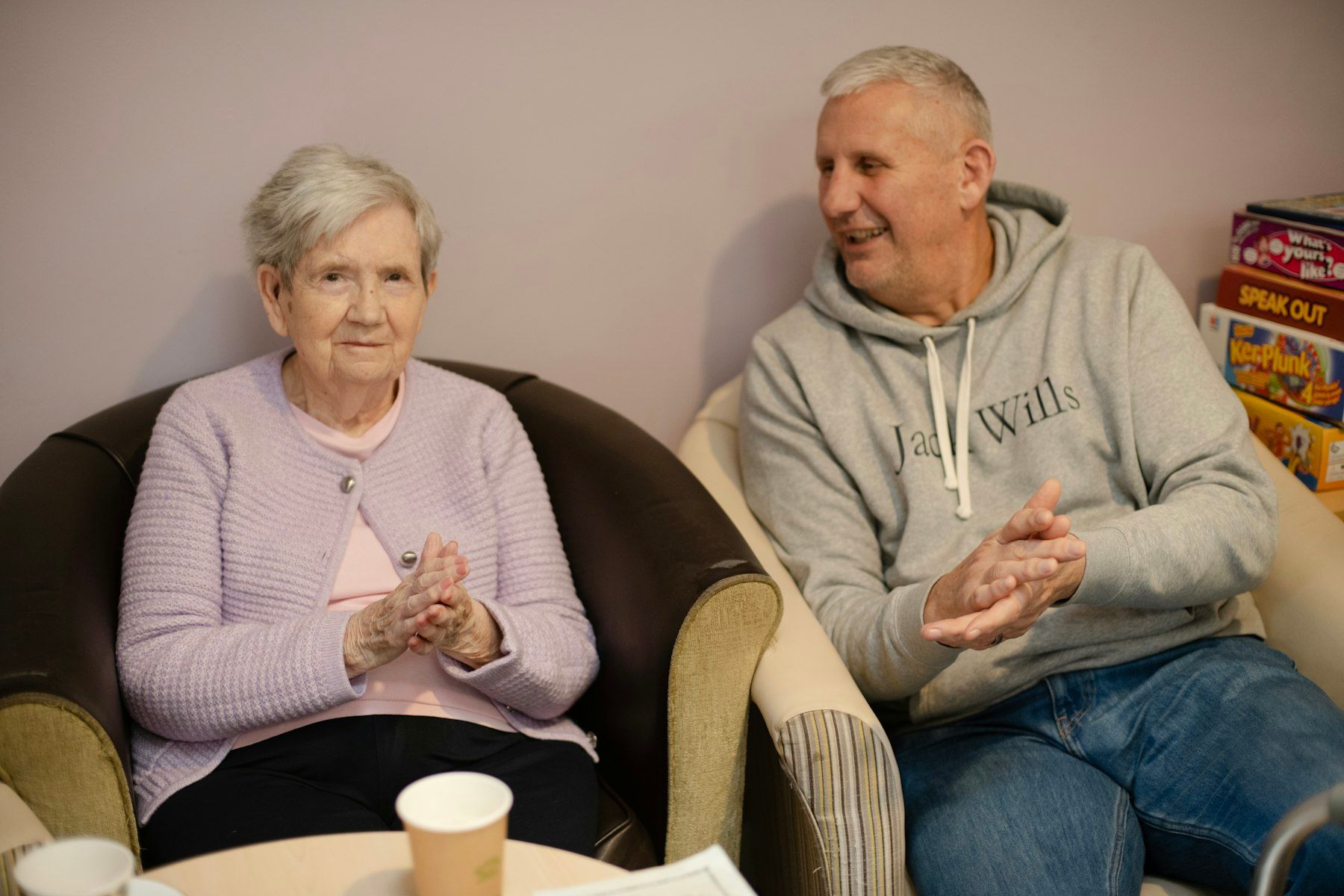 An older woman and man sit in armchairs at home, smiling