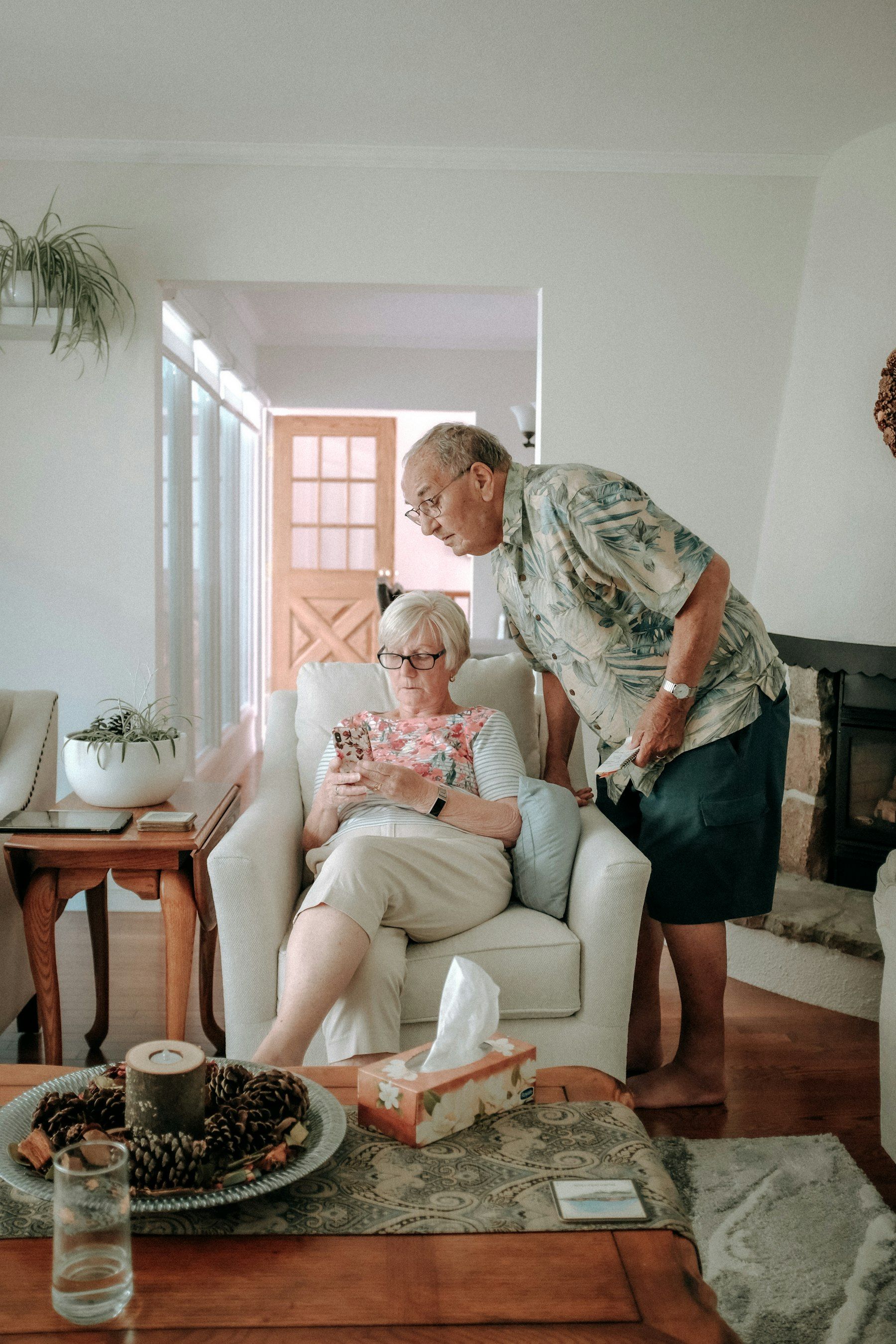 A man helps an older woman settled in her armchair at home