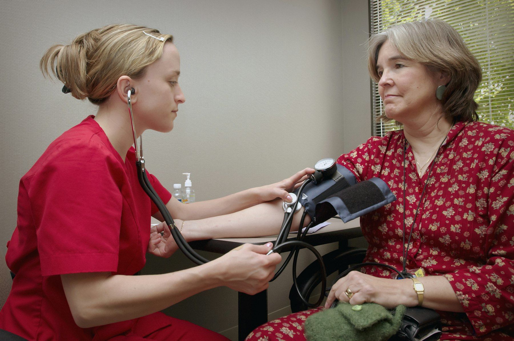A nurse takes an older woman’s blood pressure as they sit together