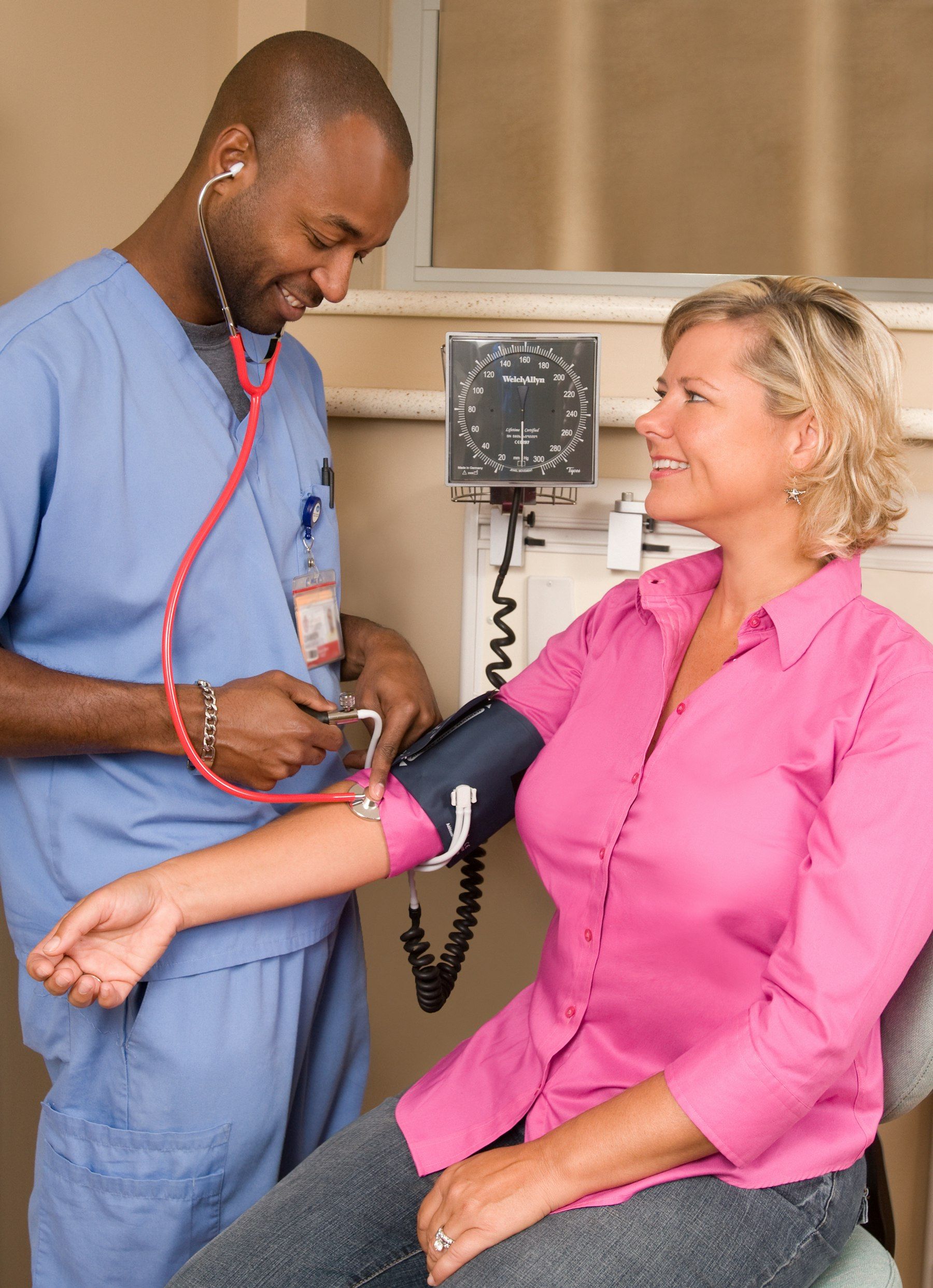 A nurse in scrubs takes a woman’s blood pressure