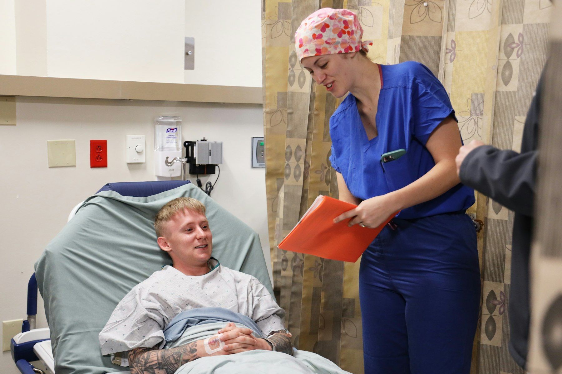 A nurse with a clipboard talks with a patient in bed