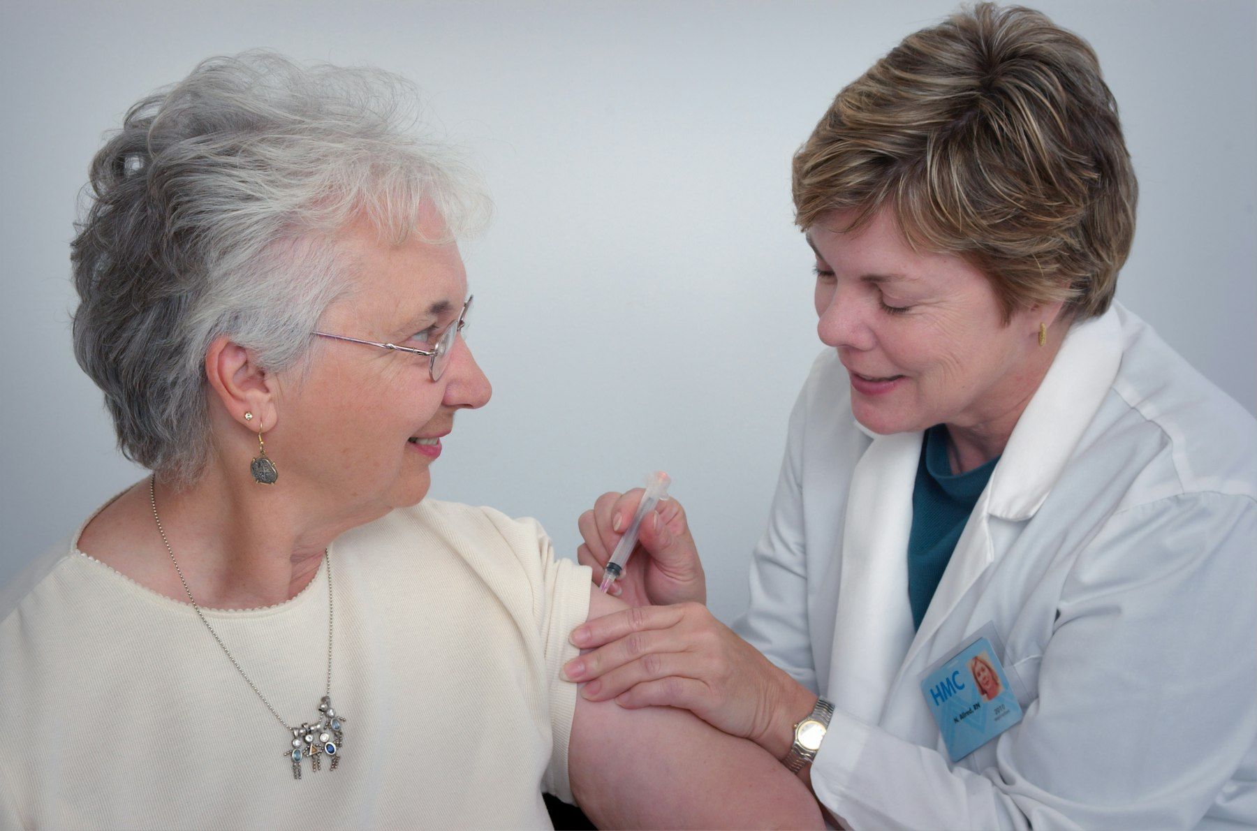 A nurse gently treats an older woman’s arm while she smiles