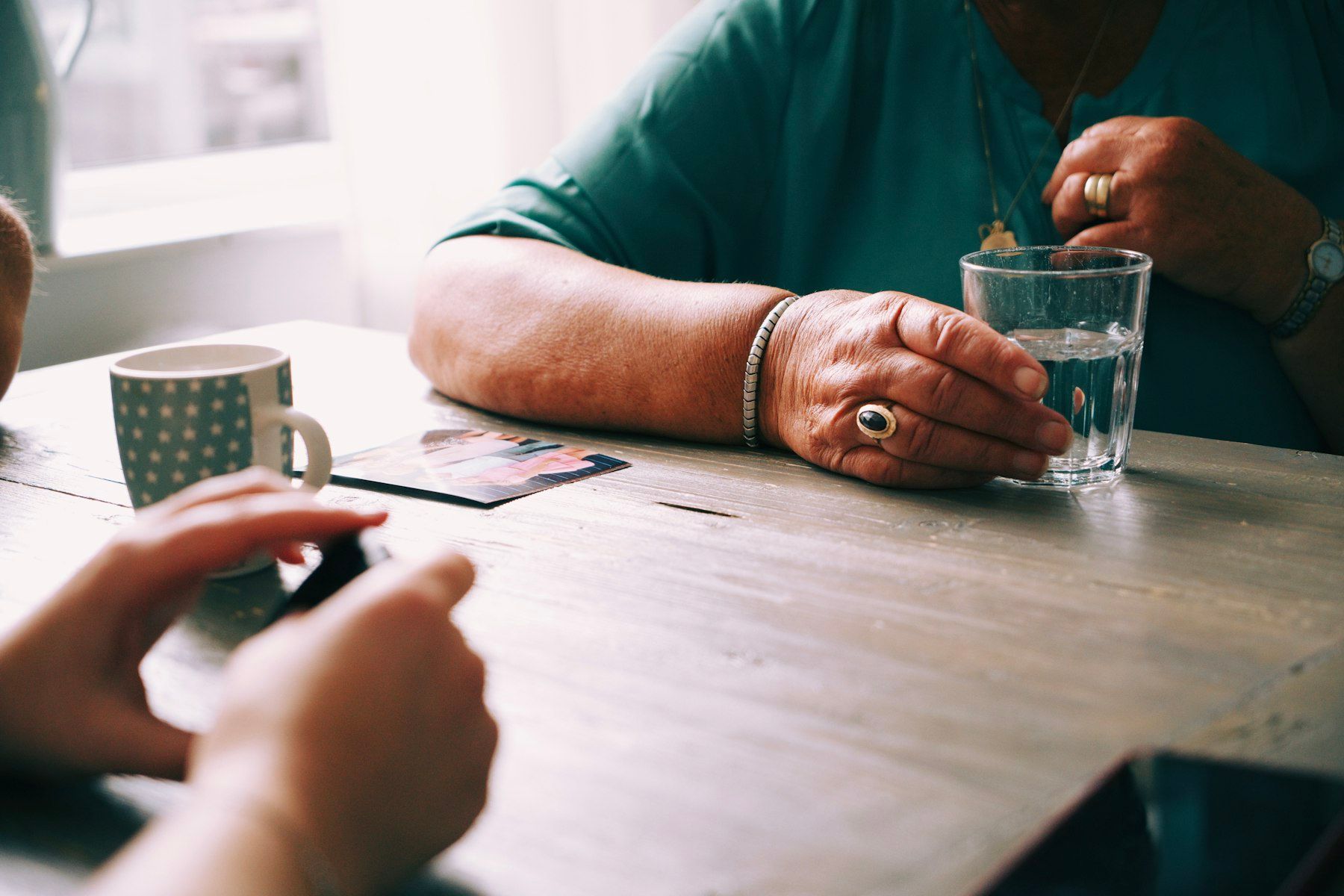 An older person holds a glass of water at the kitchen table